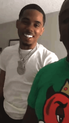 A Man In A White Shirt And A Green Shirt With A Devil On It Smiles GIF