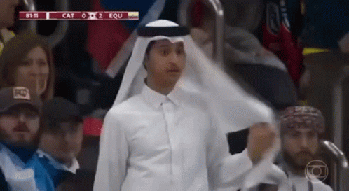 A Man In A White Shirt And A White Scarf Is Standing In A Crowd . GIF