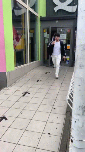 Man In White Shirt And Black Jacket Walking Down Sidewalk GIF