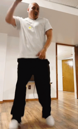 A Man In A White Shirt And Black Pants Is Dancing In An Empty Room GIF