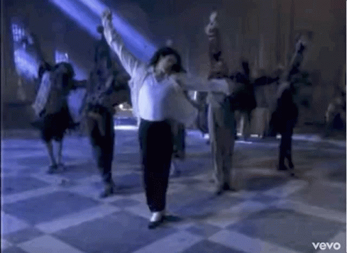 A Man In A White Shirt And Black Pants Is Dancing On A Checkered Floor With A Group Of People . GIF