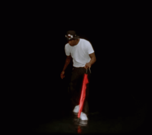 A Man In A White Shirt And Black Pants Is Holding A Red Umbrella GIF
