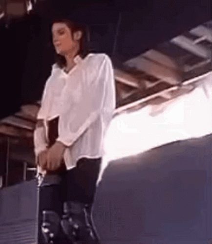 A Man In A White Shirt And Black Pants Is Sitting On A Stool . GIF