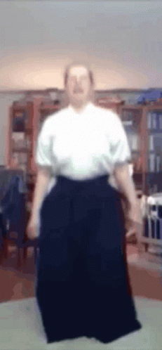 A Man In A White Shirt And Black Pants Is Standing In A Room GIF