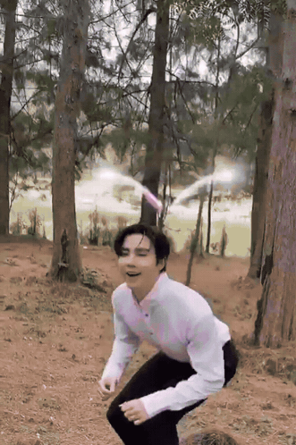 A Man In A White Shirt And Black Pants Squats In The Woods GIF