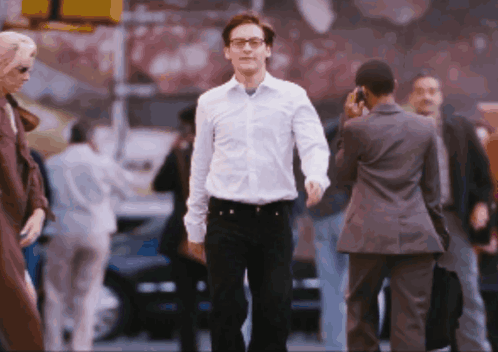 A Man In A White Shirt And Black Pants Walks Down A Street GIF
