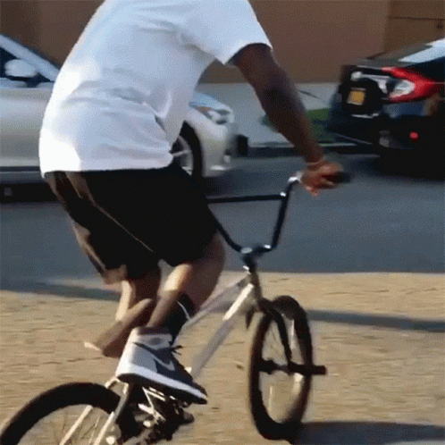 A Man In A White Shirt And Black Shorts Rides A Bike GIF
