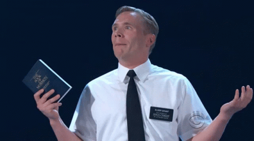 A Man In A White Shirt And Black Tie Is Holding A Book That Says " The Book Of Mormon " GIF