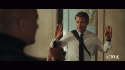 A Man In A White Shirt And Black Tie Is Holding A Gun In Front Of Another Man In A Netflix Advertisement GIF
