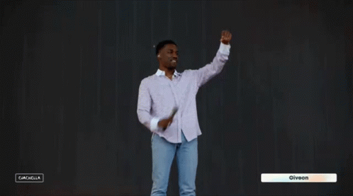 A Man In A White Shirt And Blue Jeans Is Dancing In Front Of A Black Background With The Name Giveon On The Bottom Right GIF