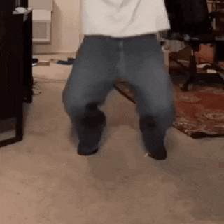 a man in a white shirt and blue jeans is jumping in the air in a living room .