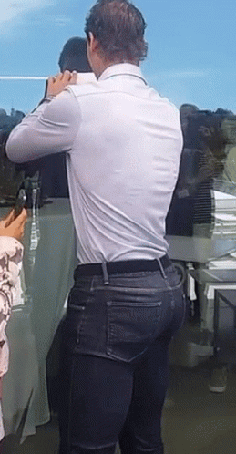 A Man In A White Shirt And Blue Jeans Is Standing In Front Of A Table GIF