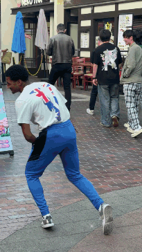 A Man In A White Shirt And Blue Pants Stands On A Sidewalk In Front Of A Neko Store GIF