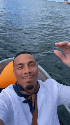 A Man In A White Shirt And Blue Scarf Is Taking A Selfie In A Boat In The Water GIF