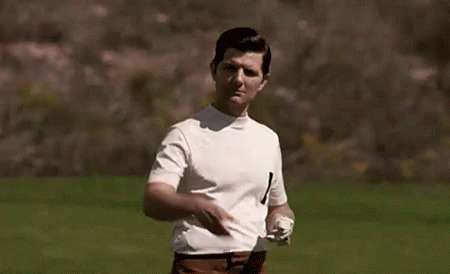 A Man In A White Shirt And Brown Pants Is Standing In A Field Holding A Golf Club . GIF