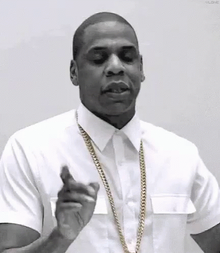 A Man In A White Shirt And Gold Chain Is Pointing At The Camera . GIF