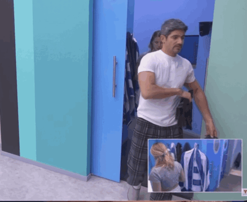 A Man In A White Shirt And Plaid Pants Stands In A Room GIF