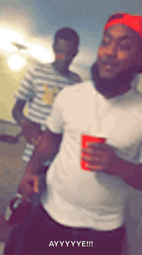A Man In A White Shirt And Red Hat Is Holding A Red Cup And Making A Funny Face . GIF