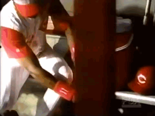 A Man In A White Shirt And Red Hat Is Holding A Red Glove With The Letter C On It GIF