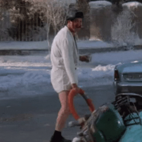 A Man In A White Shirt And Shorts Is Walking Down A Snowy Street GIF