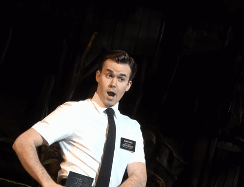 A Man In A White Shirt And Tie Is Laughing While A Woman Stands Behind Him GIF