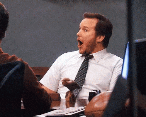 A Man In A White Shirt And Tie Is Sitting At A Desk With His Mouth Open GIF