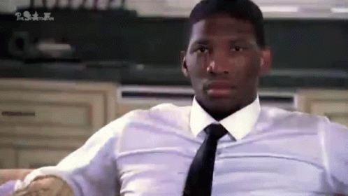 A Man In A White Shirt And Tie Is Sitting On A Couch In A Kitchen . GIF