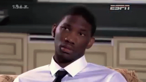 A Man In A White Shirt And Tie Is Sitting On A Couch Looking At The Camera . GIF