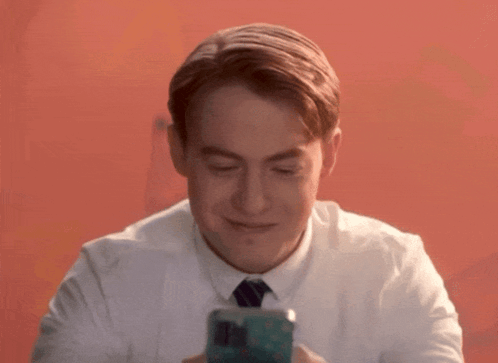 A Man In A White Shirt And Tie Is Smiling And Looking At His Phone GIF