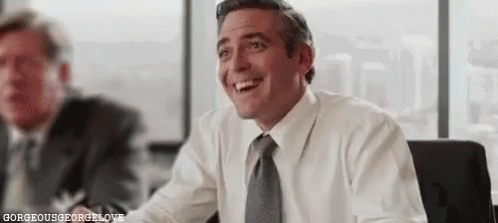 A Man In A White Shirt And Tie Is Smiling While Sitting At A Table In An Office . GIF