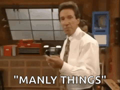 A Man In A White Shirt And Tie Is Standing In An Office Holding A Cell Phone And Saying `` Manly Things '' . GIF