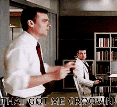 A Man In A White Shirt And Tie Is Standing In Front Of A Bookshelf And Says That Got Me Groovin ! GIF