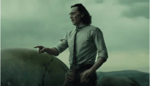 A Man In A White Shirt And Tie Is Standing Next To A Large Rock And Pointing At It . GIF