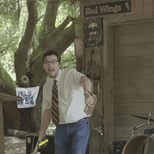 A Man In A White Shirt And Tie Stands In Front Of A Sign That Says Red Wings GIF
