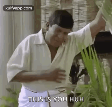 A Man In A White Shirt And White Pants Is Standing Next To A Plant And Talking To It . GIF