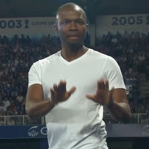 A Man In A White Shirt Applauds In Front Of A Sign That Says 003 GIF