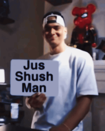 A Man In A White Shirt Holds A Sign That Says Jus Shush Man GIF