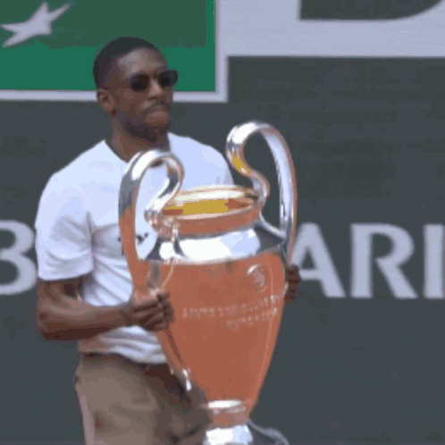 A Man In A White Shirt Holds A Trophy In Front Of A Sign That Says Rie GIF
