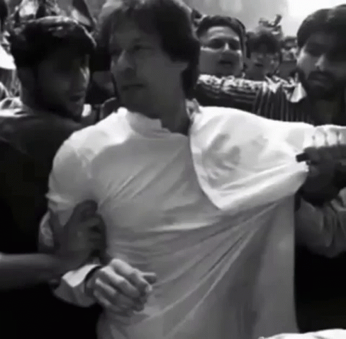 A Man In A White Shirt Is Being Pulled By A Crowd Of People GIF