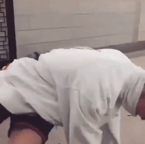 a man in a white shirt is bending over and looking down .