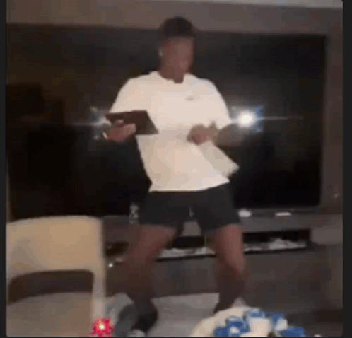 A Man In A White Shirt Is Dancing In A Living Room While Holding A Tablet . GIF