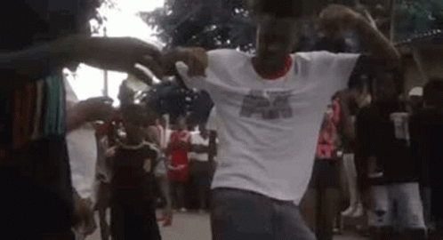 A Man In A White Shirt Is Dancing In Front Of A Crowd . GIF