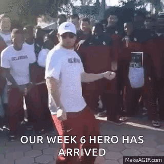 A Man In A White Shirt Is Dancing In Front Of A Crowd Of People With The Words `` Our Week 6 Hero Has Arrived '' . GIF