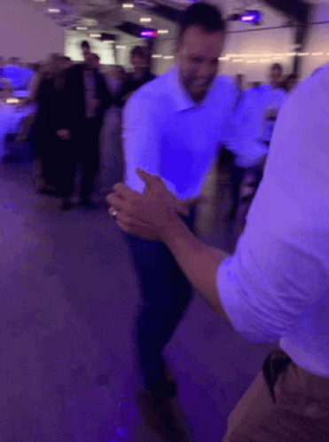 A Man In A White Shirt Is Dancing With Another Man In A Blue Shirt . GIF