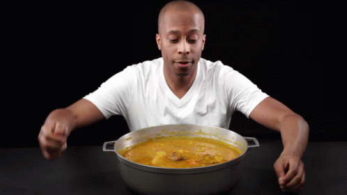A Man In A White Shirt Is Eating From A Large Pot GIF