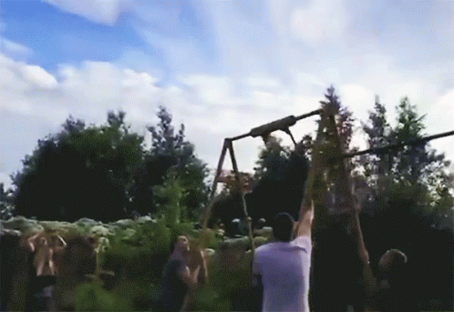 A Man In A White Shirt Is Hanging From A Rope In Front Of A Crowd Of People GIF