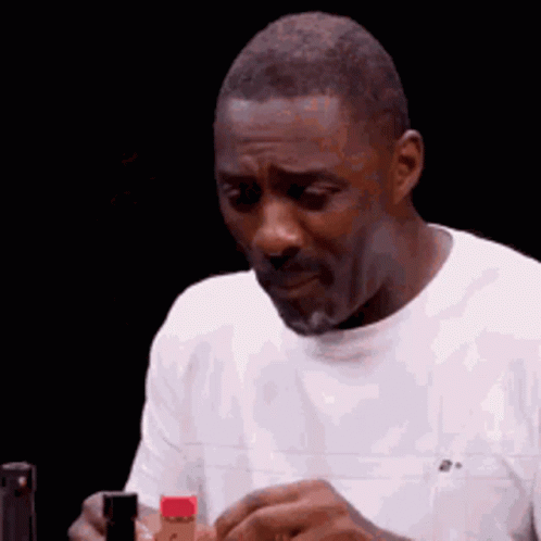 A Man In A White Shirt Is Holding A Bottle Of Hot Sauce In His Hand . GIF