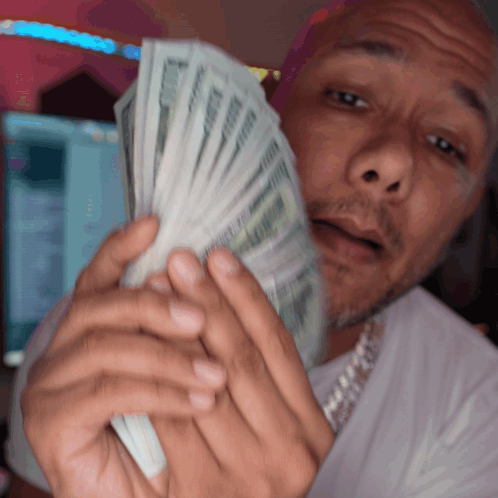 A Man In A White Shirt Is Holding A Bunch Of Money In Front Of His Face GIF