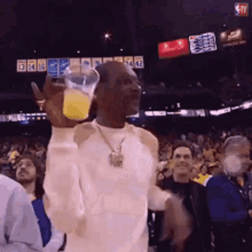 A Man In A White Shirt Is Holding A Glass Of Orange Juice In His Hand GIF