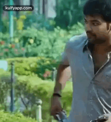 A Man In A White Shirt Is Holding A Gun In His Hand . GIF